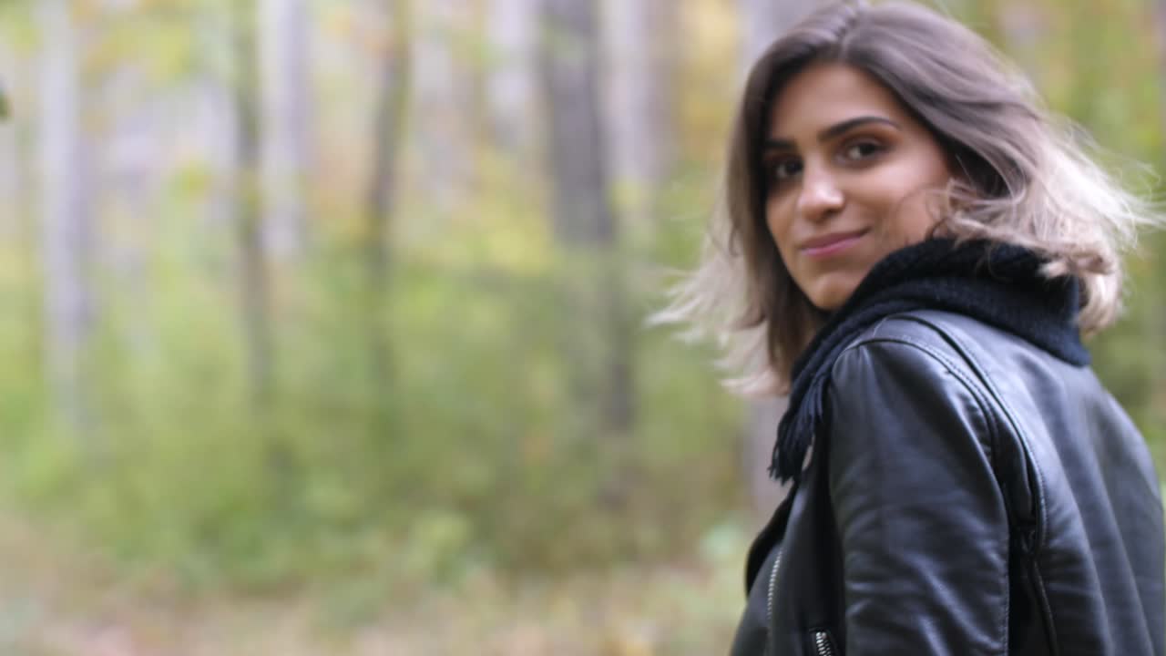 primer plano por detrás de una chica morena en el bosque de otoño, caminando y sonriendo a la cámara