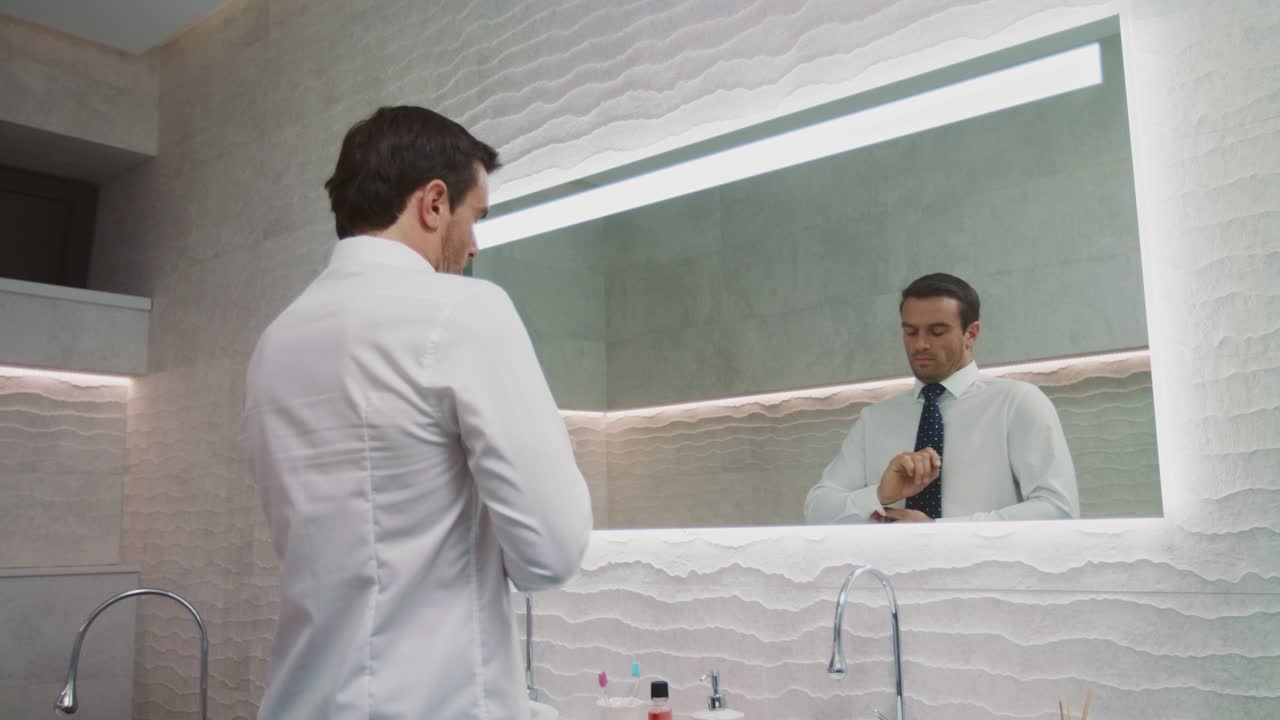 Uomo d'affari che si sistema la cravatta in un bagno di lusso. Uomo felice che indossa la cravatta in casa.