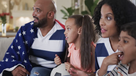 Aufgeregt-Gemischtrassige-Eltern,-Sohn-Und-Tochter-Mit-Amerikanischer-Flagge-Beim-Sportschauen-Im-Fernsehen,-Zeitlupe