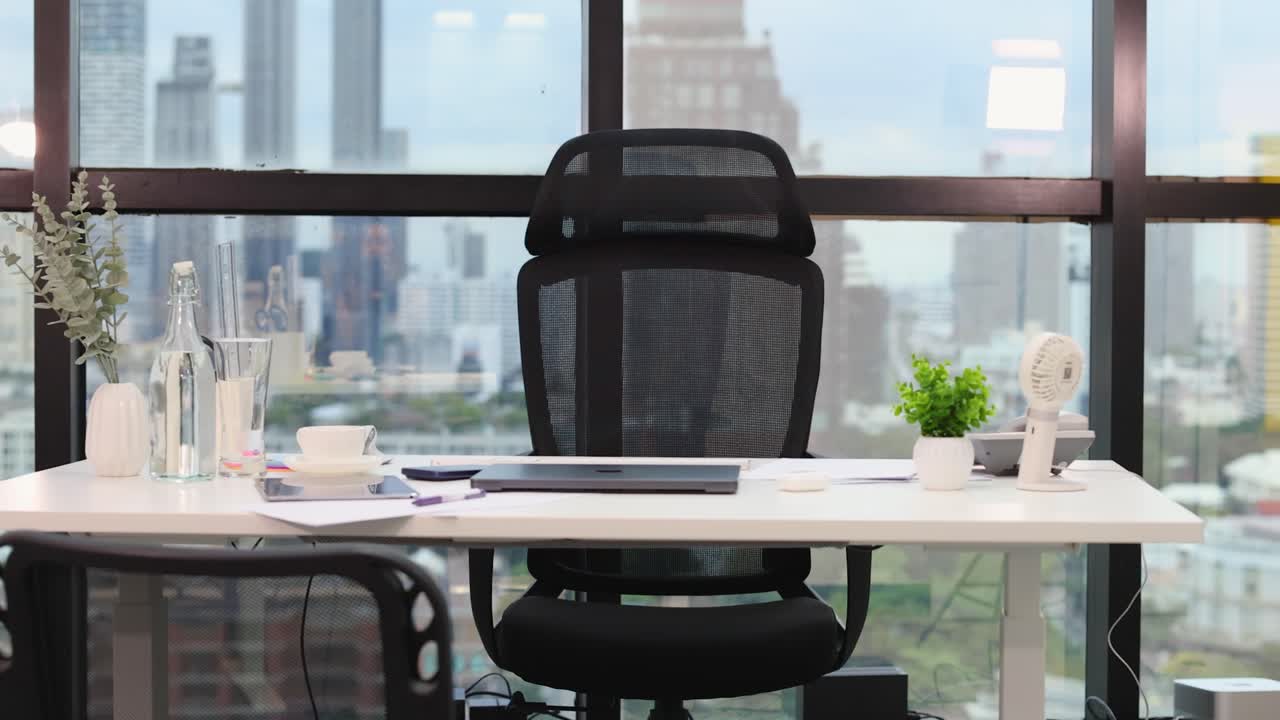 Camera smoothly dollies and pans across a bright, empty office desk overlooking urban skyscrapers