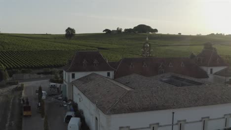 prestigious château angélus winery at sunset, sun flare shines over estate and vineyards in saint-émilion, bordeaux region of france. aerial backward