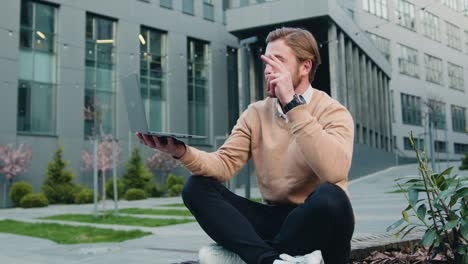 businessman male freelancer using laptop having video call outdoors. male caucasian makes conference chat using new technology sitting modern building background
