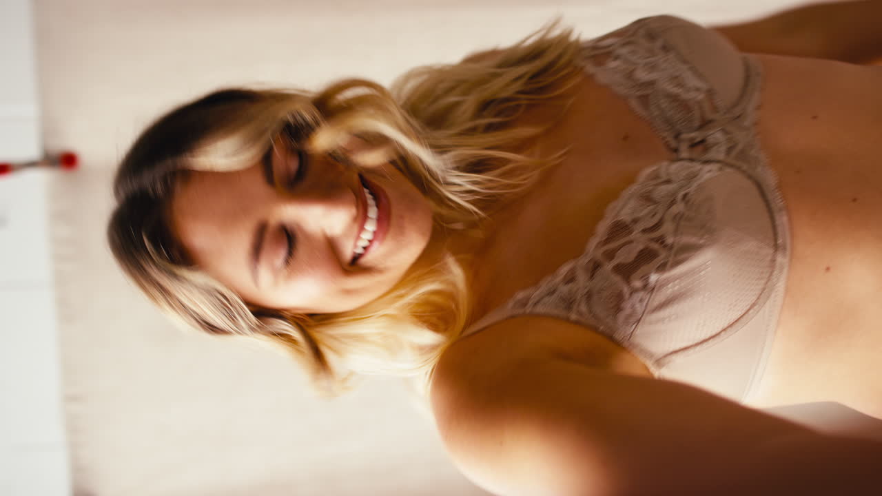 Video verticale POV: Ripresa in studio di donna naturale e sicura di sé in biancheria intima che balla e posa per un selfie.