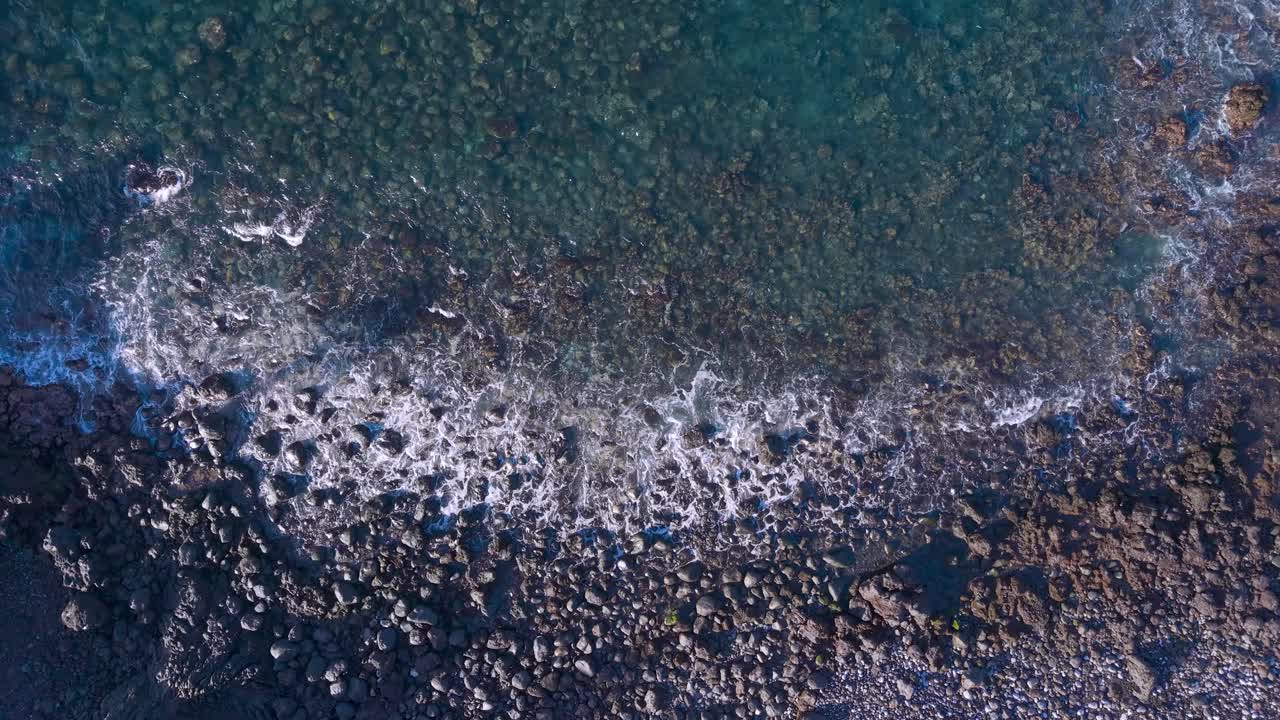 Aerial view of ocean waves crashing on a rocky coastline at sunrise
