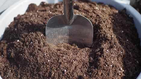 close up of potting soil in a flower pot with a hand trowel