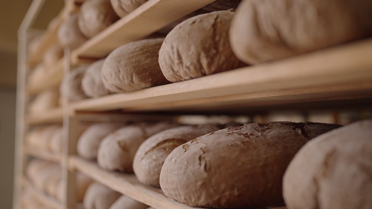 Freshly baked bread loaves on wooden shelves in bakery, artisanal bread production.