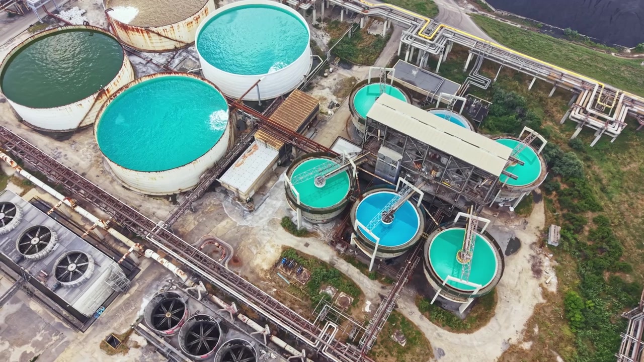 Large industrial facility with water tanks and pipes located near a green area showing tanks used for processing