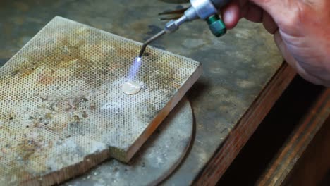 close-up of craftswoman blowing a torch to melt metal