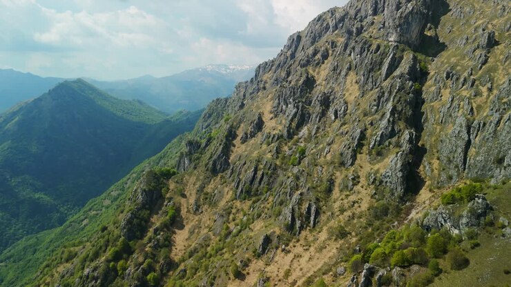 Vuelo aéreo lento pasando por un paisaje de picos montañosos rocosos y verdes en los Alpes italianos.