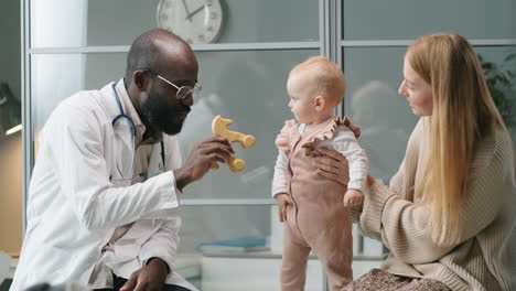 pediatrician playing with baby girl and talking to mother in clinic