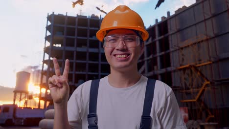 un trabajador asiático muestra un gesto de paz a la cámara en el sitio de construcción