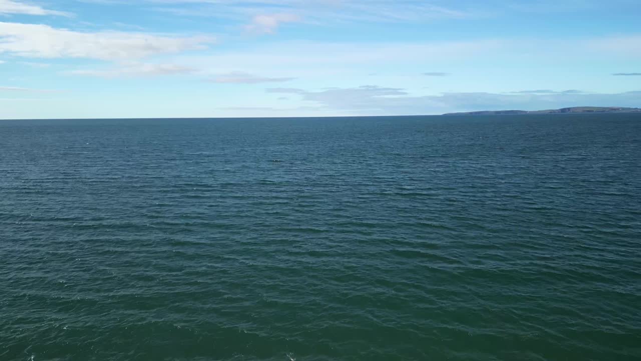 Drone flight over sandy beach straight over ocean waves and towards horizon. Sunny Ireland