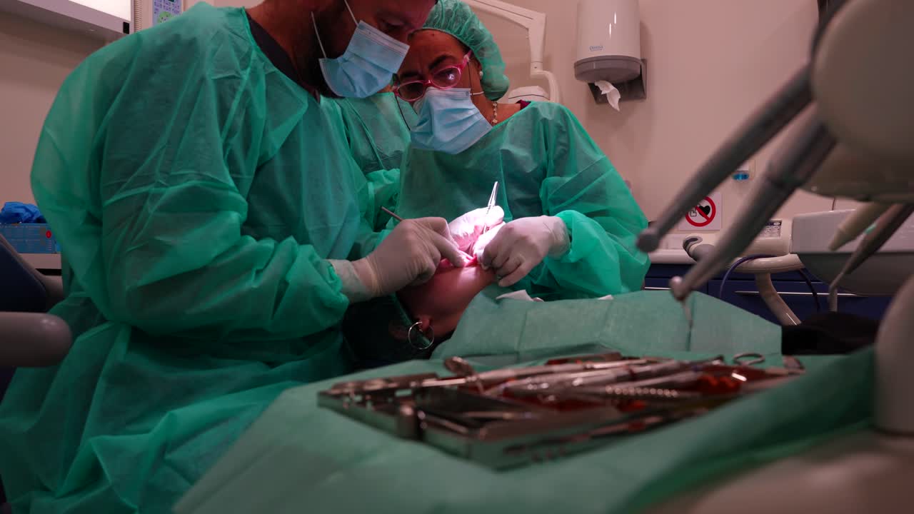 fotografía media de un equipo de odontólogos preparando una cirugía de injerto dental mientras el asistente sostiene el labio inferior del paciente