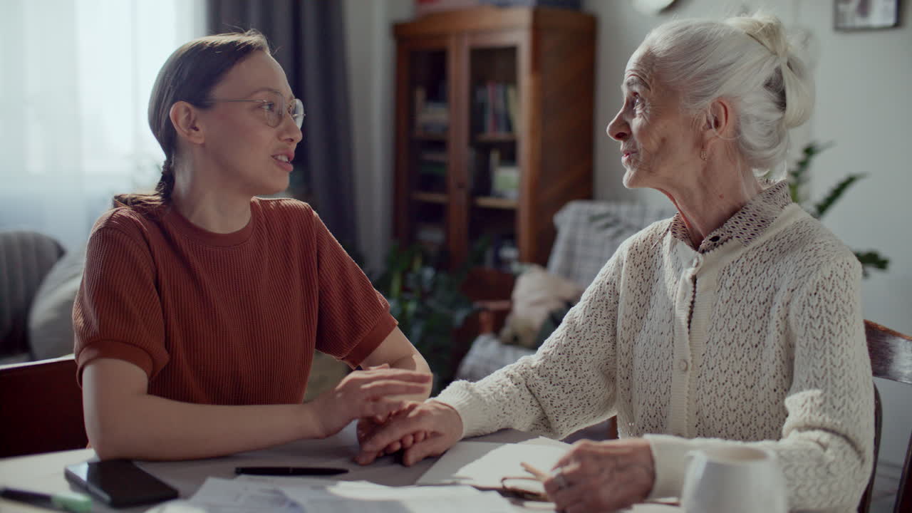 Young Woman Holding Hand of Elderly Grandmother during Conversation at Home