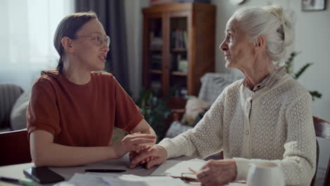 young woman holding hand of elderly grandmother during conversation at home