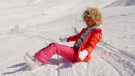 Woman-in-orange-snowsuit-sitting-on-ski-slope