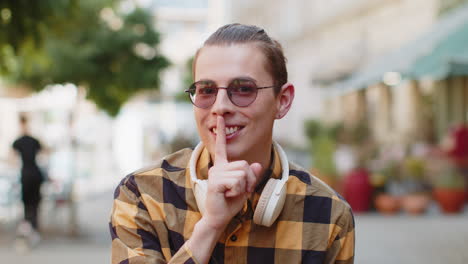 young man presses index finger to lips making silence hush gesture sign do not tells gossip secret