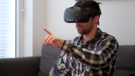 un disparo medio de un joven blanco jugando a la realidad virtual mientras está sentado en un sofá sin controladores