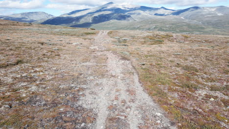 mountain-trail-path,-drone-aerial-shot-with-glacier-snow-tops-on-the-horizon