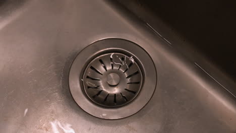 Water-drains-through-stopper-from-stainless-steel-kitchen-sink,-detail