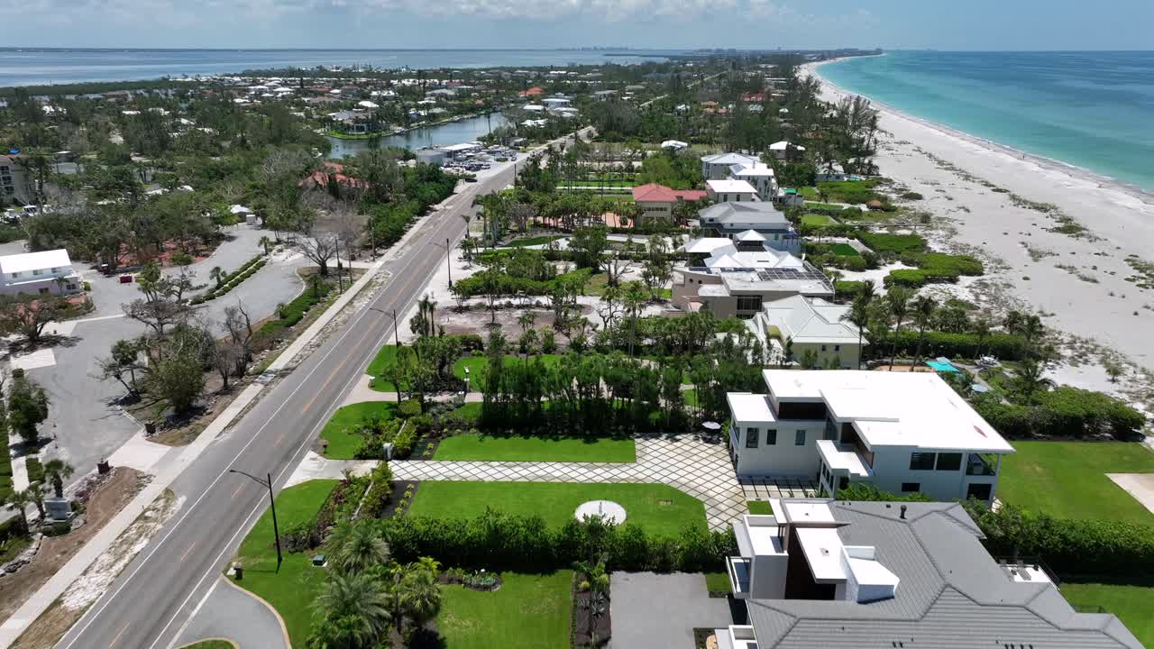Hotels and Luxury Houses with traffic on main street of Bradenton beach. Jetty with turquoise golf of mexico and blue bay on other side. Aerial forward shot. Coquina Sandy beach with villas.