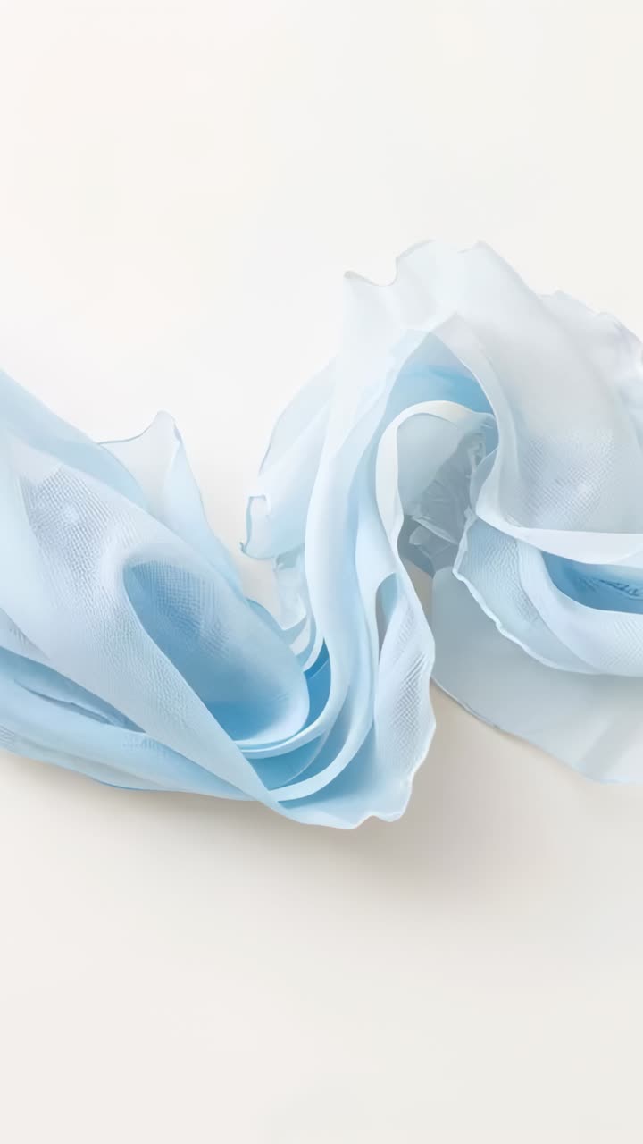 Vertical video: Unfurling pale blue chiffon scarf sliding on white tabletop, showing soft ripples