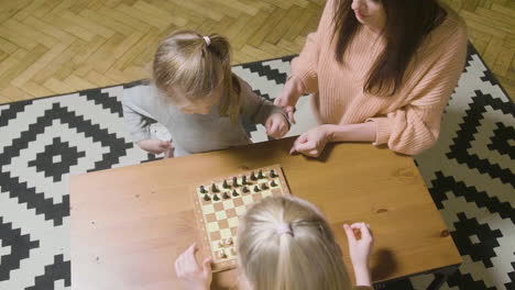 top view of mother and her two little daughters playing chess at home