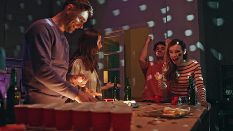 people enjoy beer pong competition at home party. man tossing ball rejoicing win