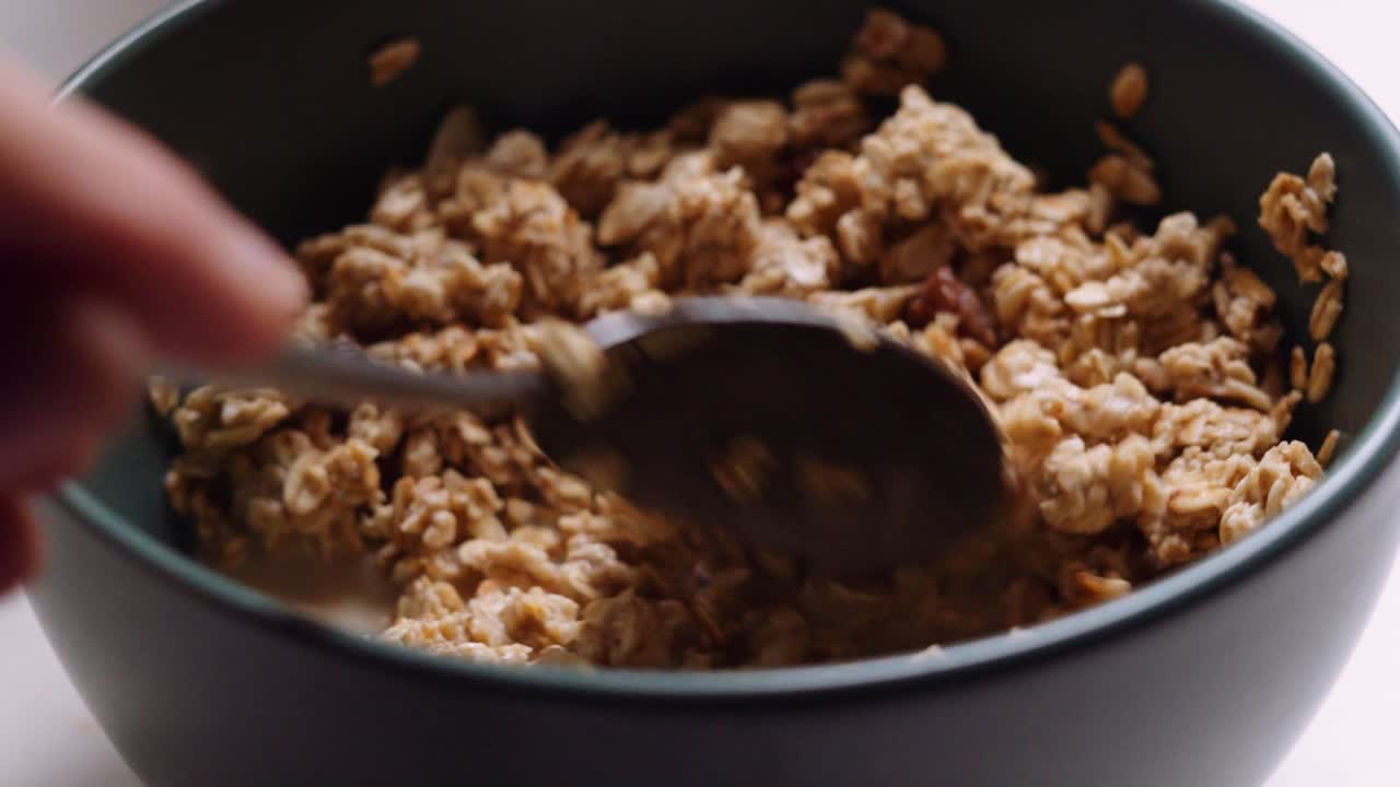 Primo piano di una ciotola di granola con mandorle e uvetta che viene mescolata e prelevata.
