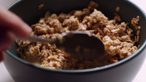 close up bowl of almond and raisin granola being stirred and picked up