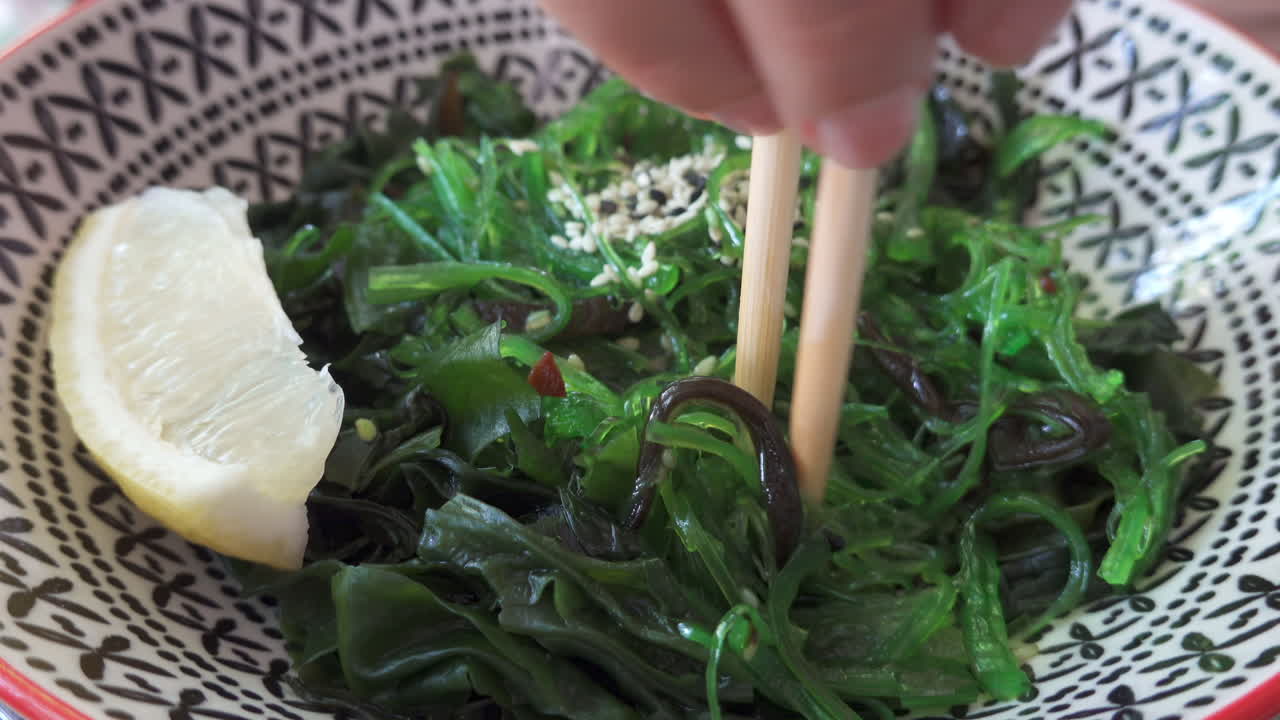 Close up of a woman eating a seaweed salad with lemon with chopsticks