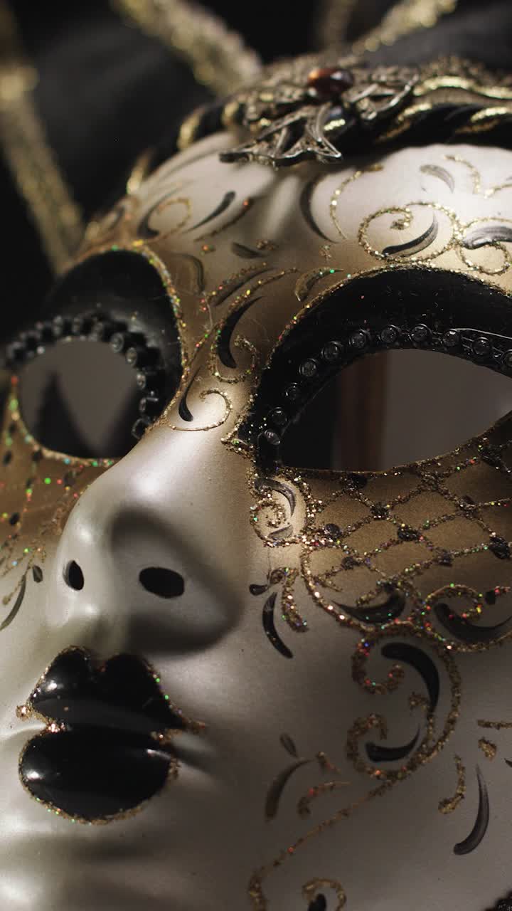Primo piano di una maschera di carnevale veneziana oro e argento che ruota sotto la luce dello studio.
