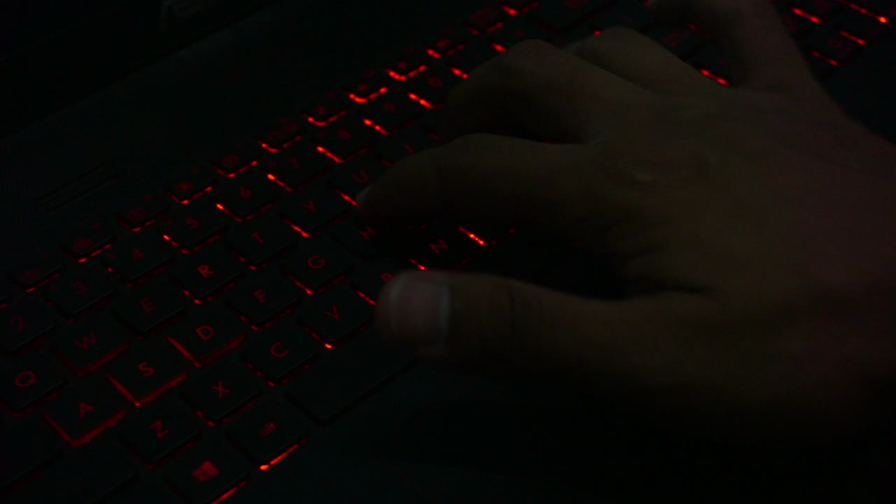 Top view of hand typing on red lighting keyboard of laptop in dark room,close up shot-1