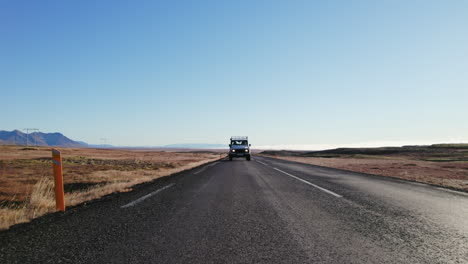 land rover defender blanco conduciendo por una carretera vacía en el sur de islandia durante la puesta de sol