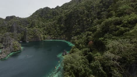 fpv drone flyover forested hillside revealing turquoise water bay in coron, philippines