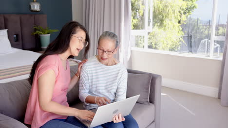 Using laptop, Asian grandmother and granddaughter sitting on couch, discussing something together