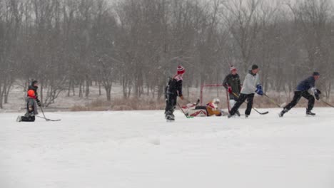 wide angle following shot of group of teenagers, children and adults playing pond hockey. they are playing on a frozen lake and it's snowing a lot.
