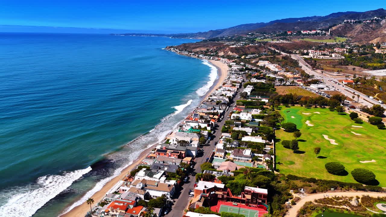 Flying over the rows of houses on the shore of the Pacific Ocean. Waves gently roll to the empty beach. Malibu, Los Angeles County, California, USA