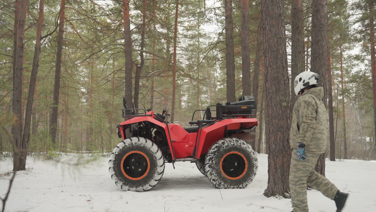 L'avventura in ATV nella foresta innevata inizia mentre il pilota si avvicina al quad rosso e sale. Il motore si avvia e i pneumatici mordono la neve fresca, nuove tracce sul tappeto di pini, acceleratore innestato e movimento che aumenta, inverno dinamico.