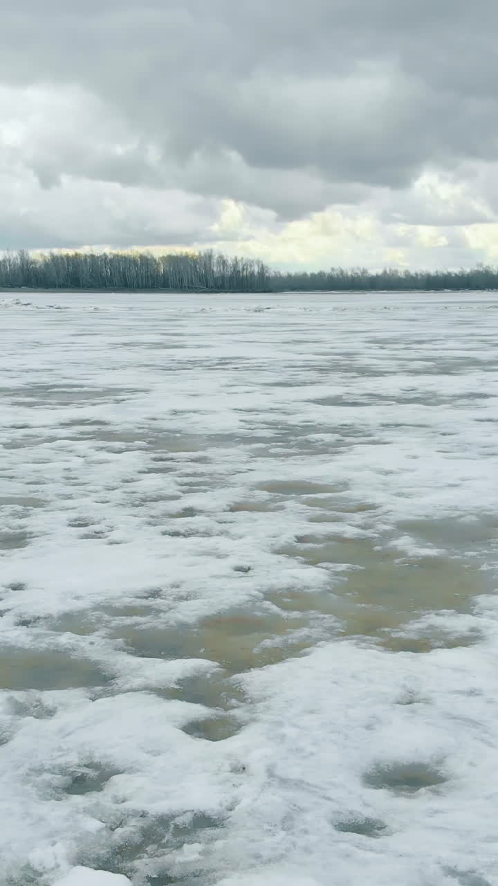 half frozen river covered with white snow against dense forest on horizon under cloudy sky upper view