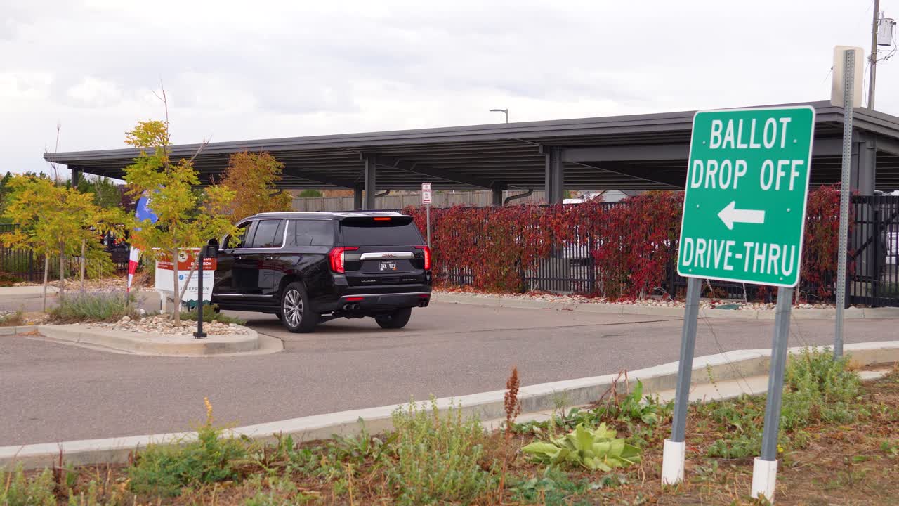 Men vote safely and conveniently from their cars by submitting mail-in ballots into secure ballot drop boxes, demonstrating civic responsibility, democracy, election integrity, and accessibility