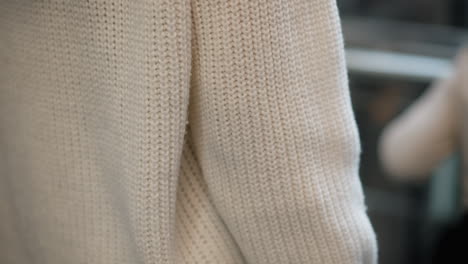 back view of refined shopper from head to waist on moving walkway in mall, pastel hair in white knit sweater holding shopping bag, motion blur capturing ambient lights and travelator rails