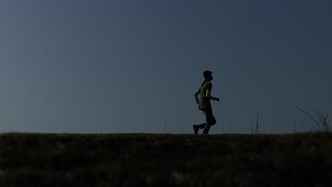 young guy running in the evening appearing on the left and running across the screen to the right in the dark with grass in the foreground and blue sky in the background