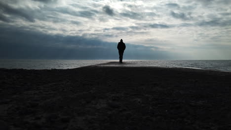 man in a black coat walking on a concrete jetty to the infinite horizon of lake ontario