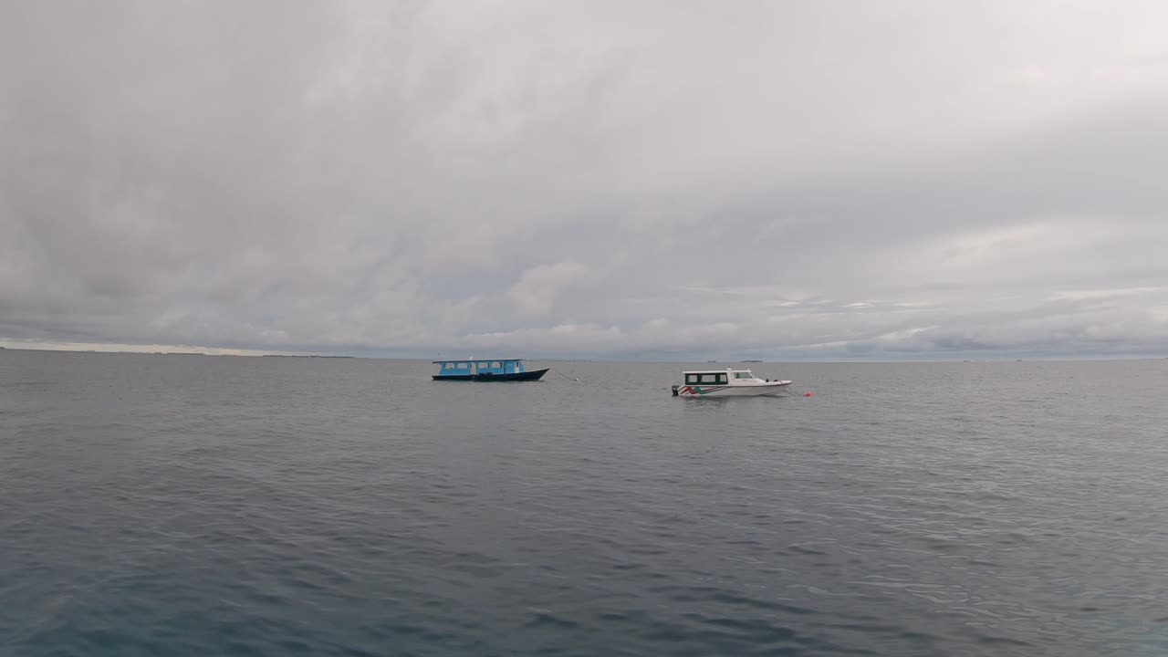 Boats on gentle sea waves at overcast sky background during quiet dusk, Maldives