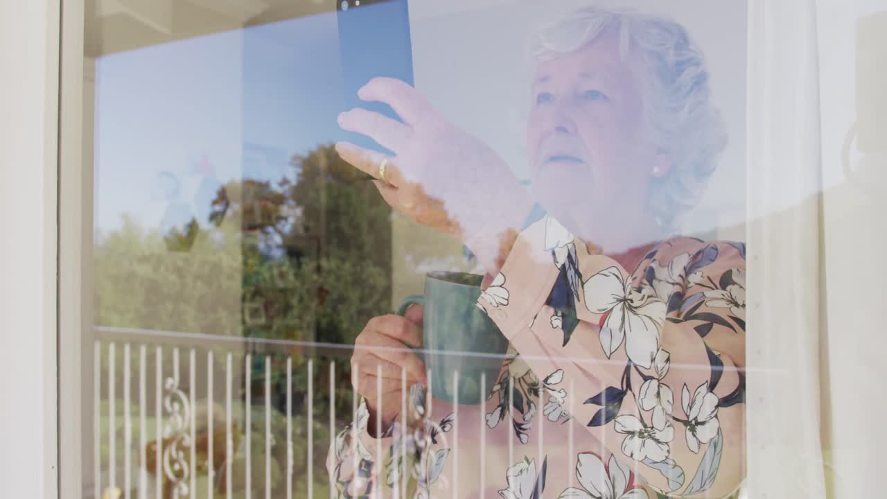 Caucasian senior woman holding coffee cup taking a picture from smartphone through the window