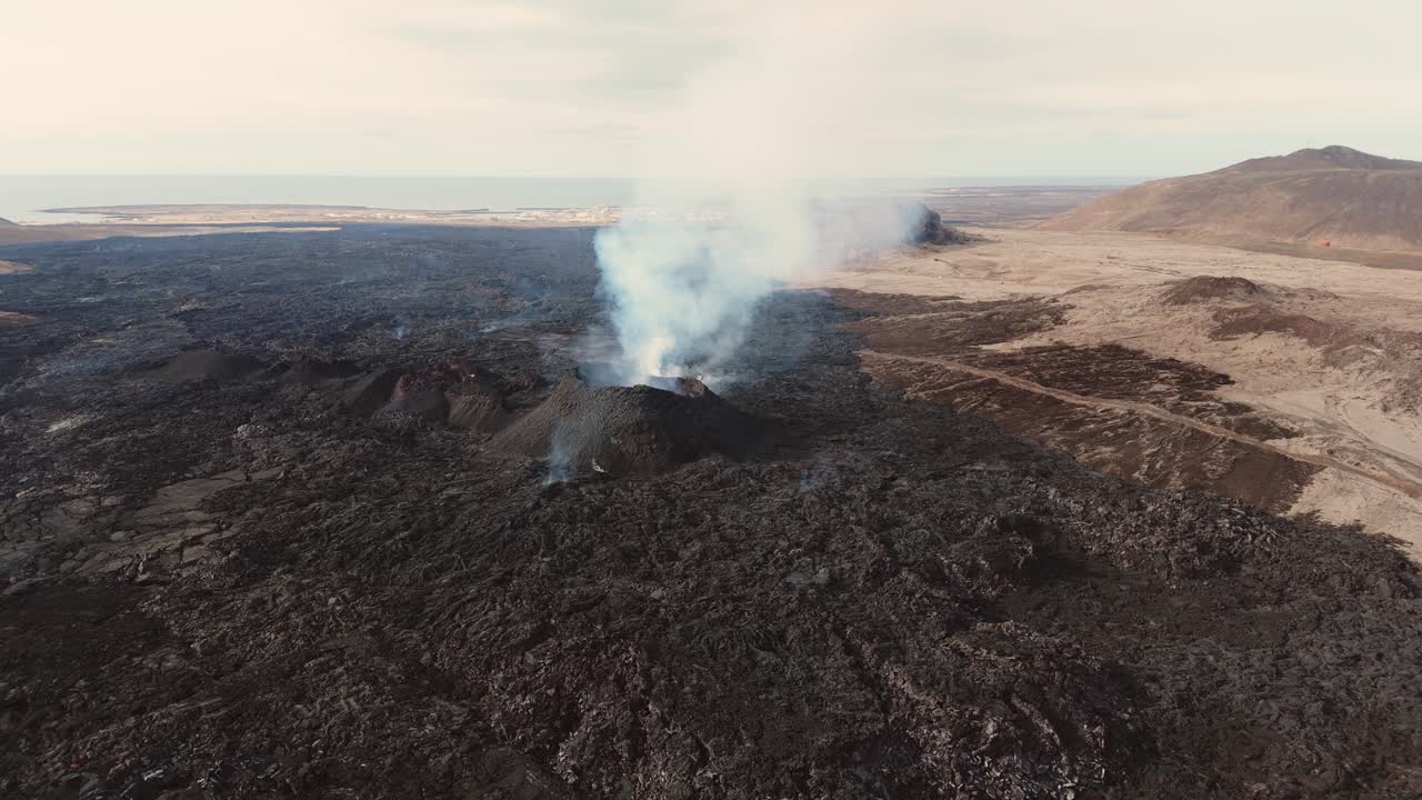 paisaje volcánico de roca negra con un volcán activo en erupción en islandia