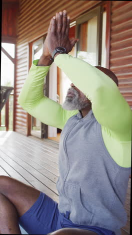 vertical video of happy senior african american man spending time in log cabin, metidating