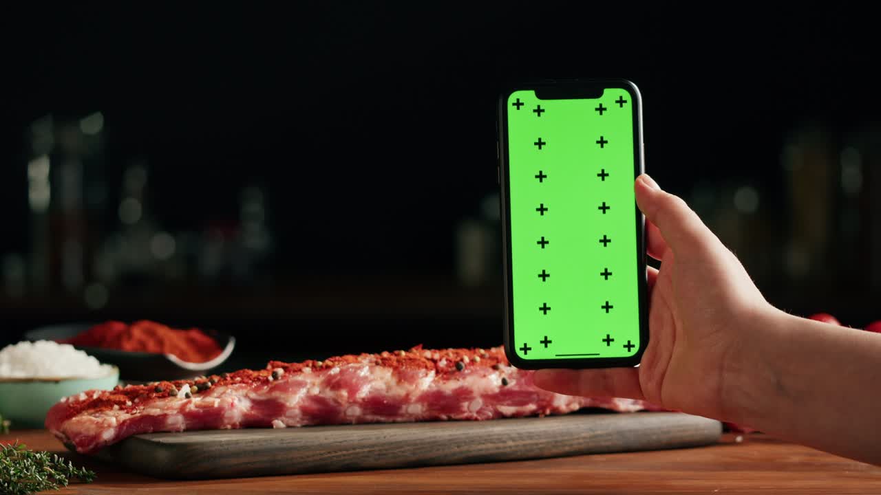 mujer chef cocinando costillas en primer plano. chef profesional preparando carne de cerdo en la cocina del restaurante, sosteniendo un teléfono inteligente con pantalla de tecla croma. deliciosa carne de cerda de barbacoa, cocina picante mexicana, comida india.