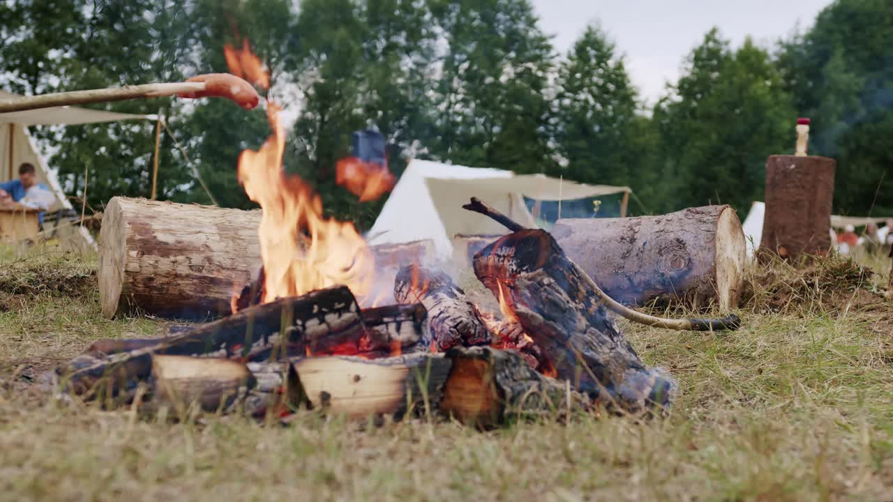 나무 막대기로 꼬챙이에 꿰인 벽난로에서 소시지를 요리하는 사람들의 정적인 클로즈업